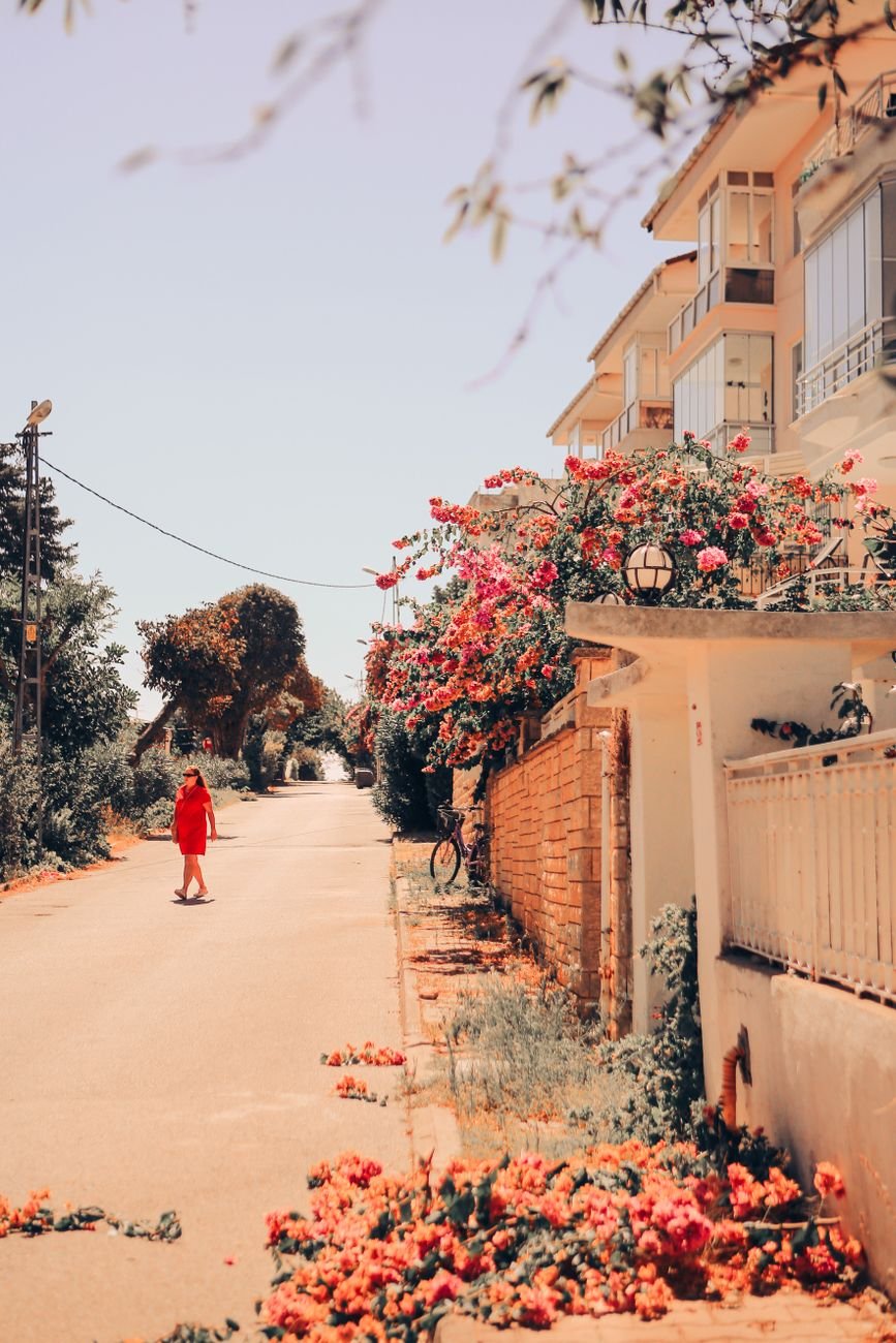 Woman in red dress walking on a summer street adorned with vibrant bougainvillea flowers.